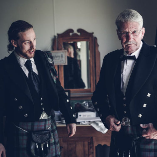 Two men in formal attire standing in a room with a mirror and furniture.